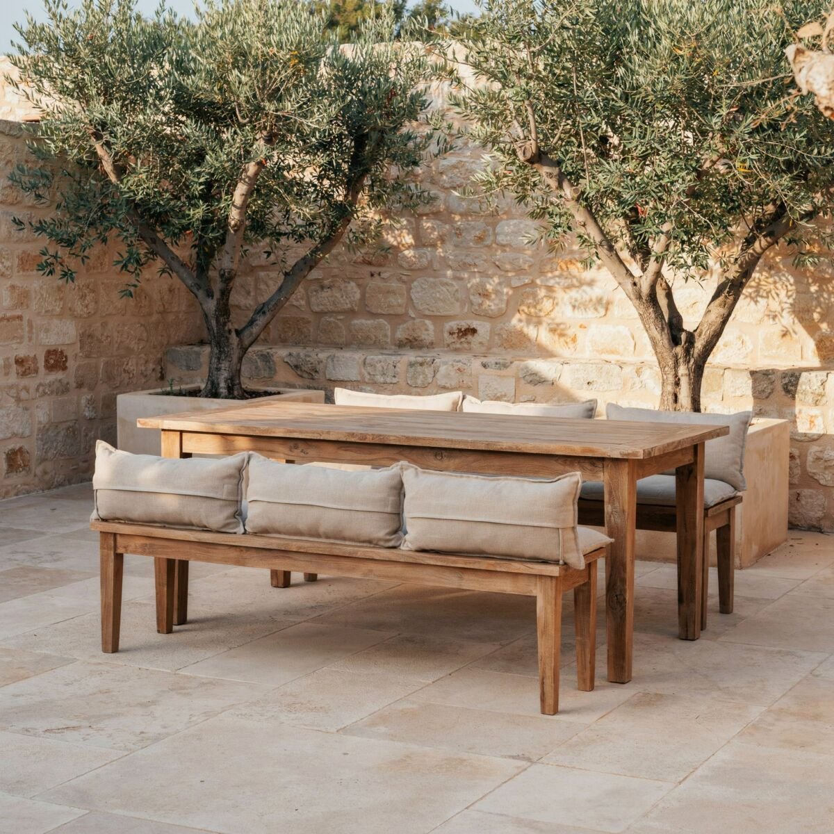 Sunlit stone terrace with an oak dining table and olive trees