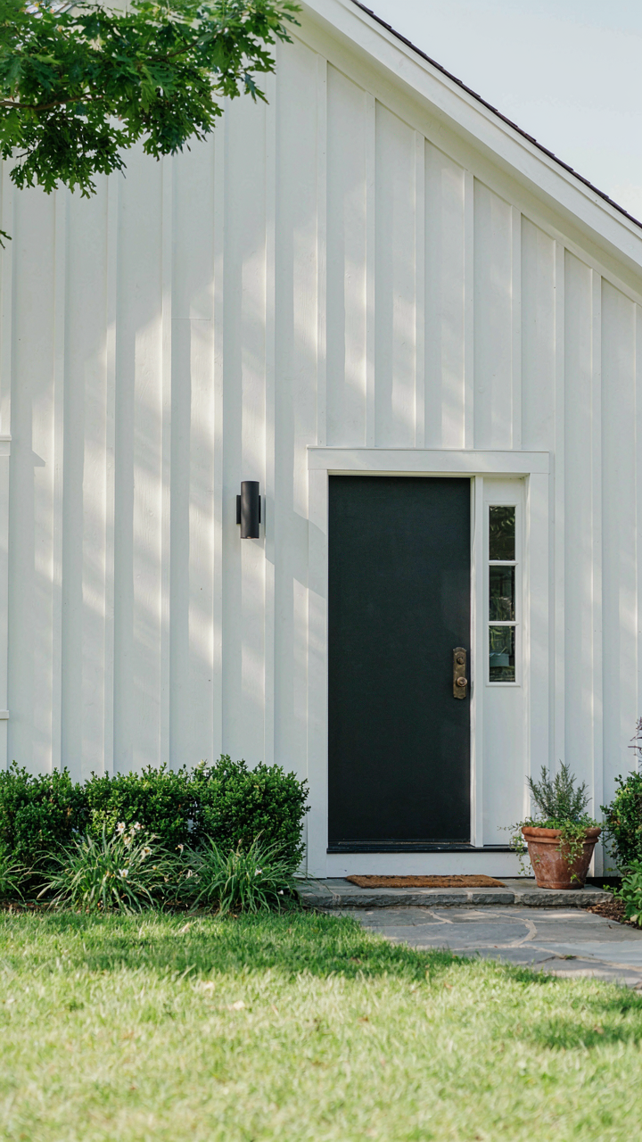 A simple white farmhouse exterior with minimal trim and dark door.