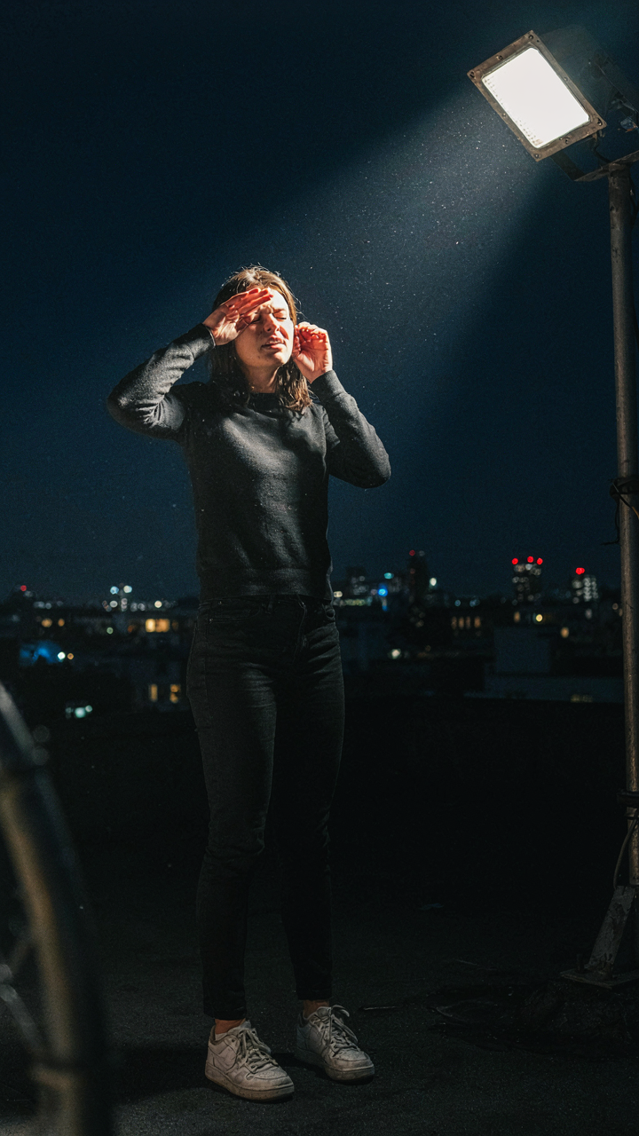 A person shields their eyes from an overly bright floodlight at night.