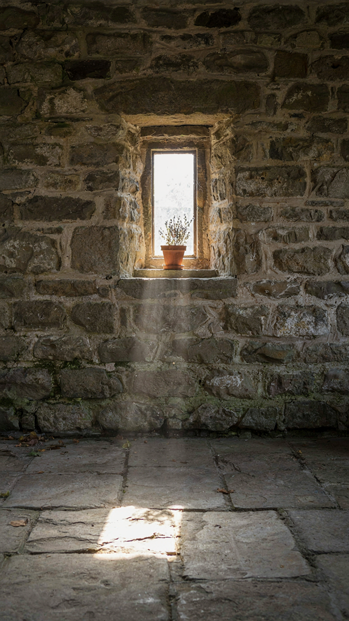 Sunlight streams through a small, deep window in a thick stone wall.