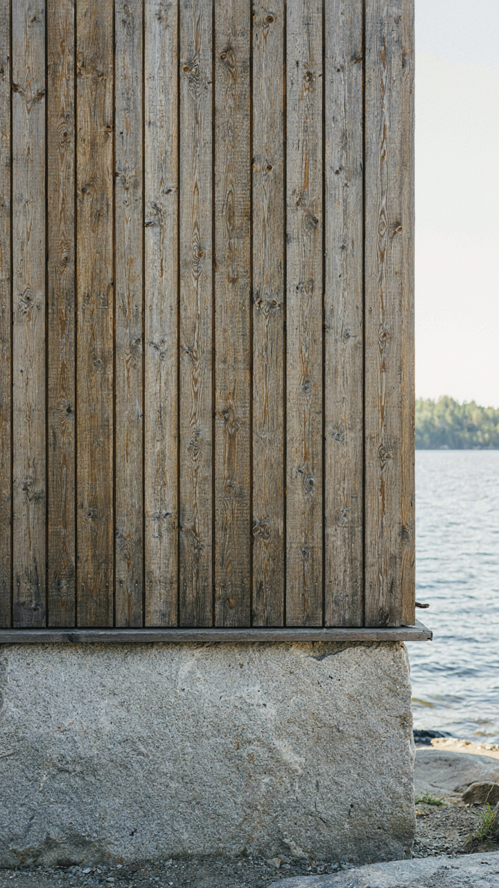 Weathered larch wood siding meets a smooth granite foundation on a lake house exterior.