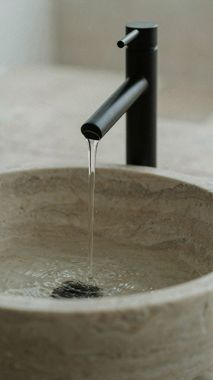 A modern faucet pours water into a natural stone basin.