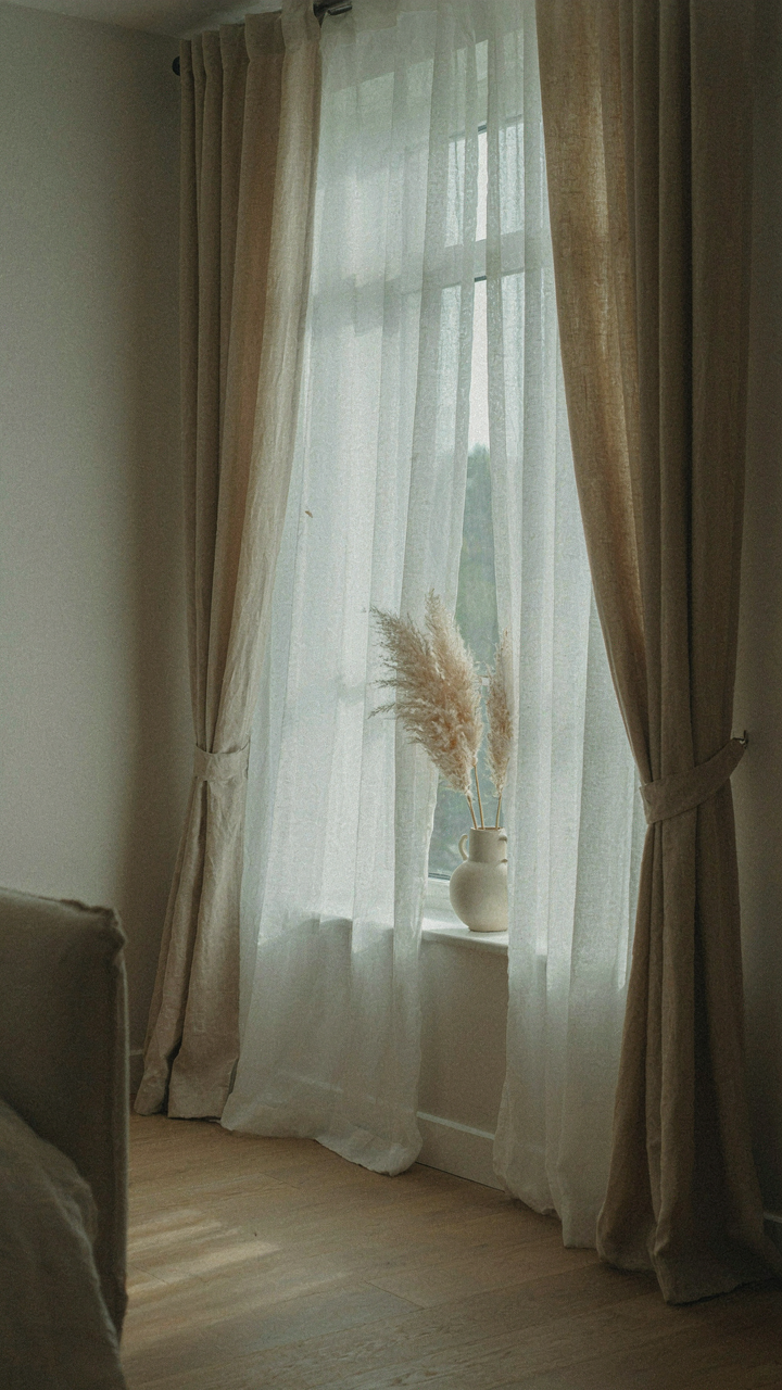 A window with sheer white curtains layered under thick linen blackout curtains.