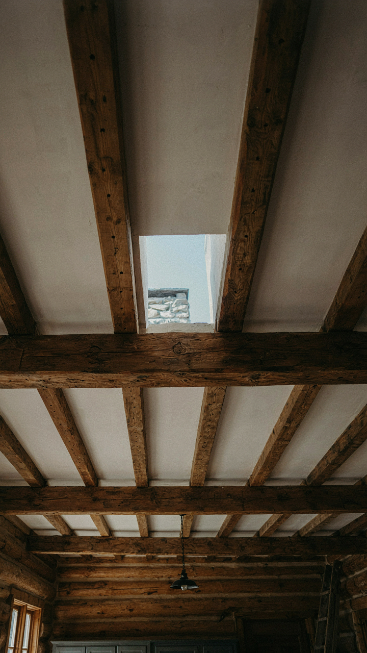 Exposed timber beams with visible grain and nail holes in a log cabin kitchen ceiling.