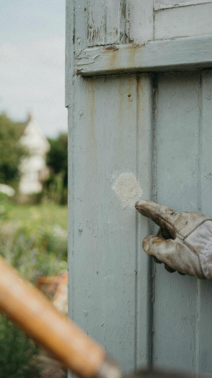 A gloved hand inspecting a small, chalky patch on a light cottage wall.