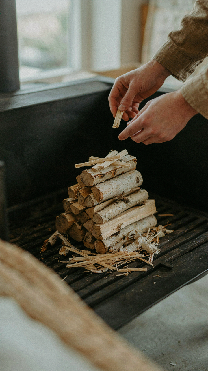 A person carefully arranging kindling and logs in a firebox.