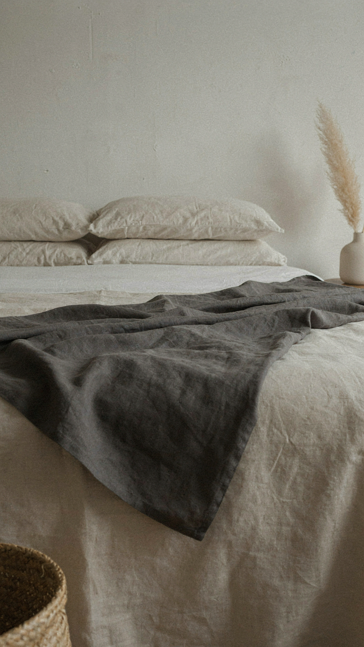 A charcoal linen throw blanket on a cream bed, showing subtle contrast.