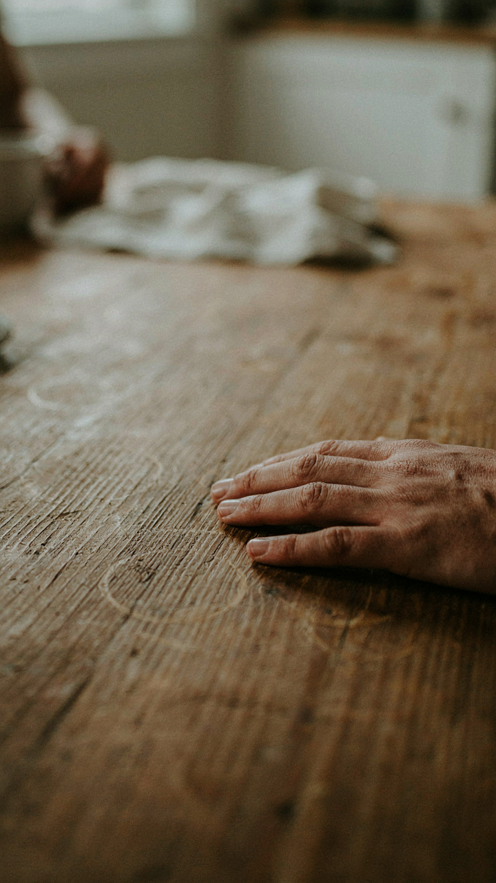 A hand gently touches the visible grain of an old oak dining table.