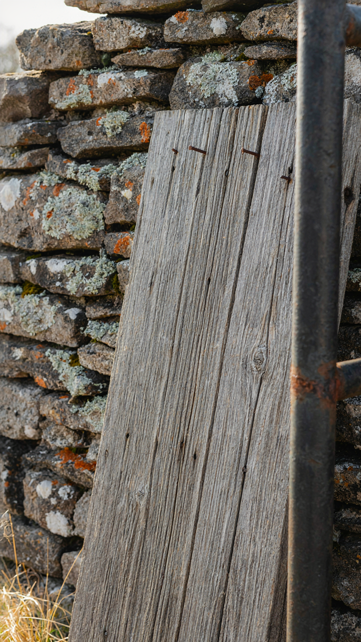 A close-up of reclaimed barn wood, a weathered fieldstone wall, and a steel railing.