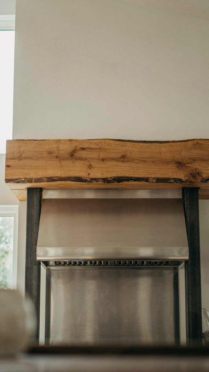 A wooden mantelpiece contrasts with a metal range hood and posts.