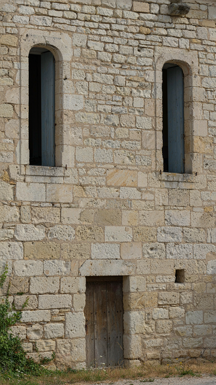 A thick, plain stone wall of a French country house with deep window recesses.
