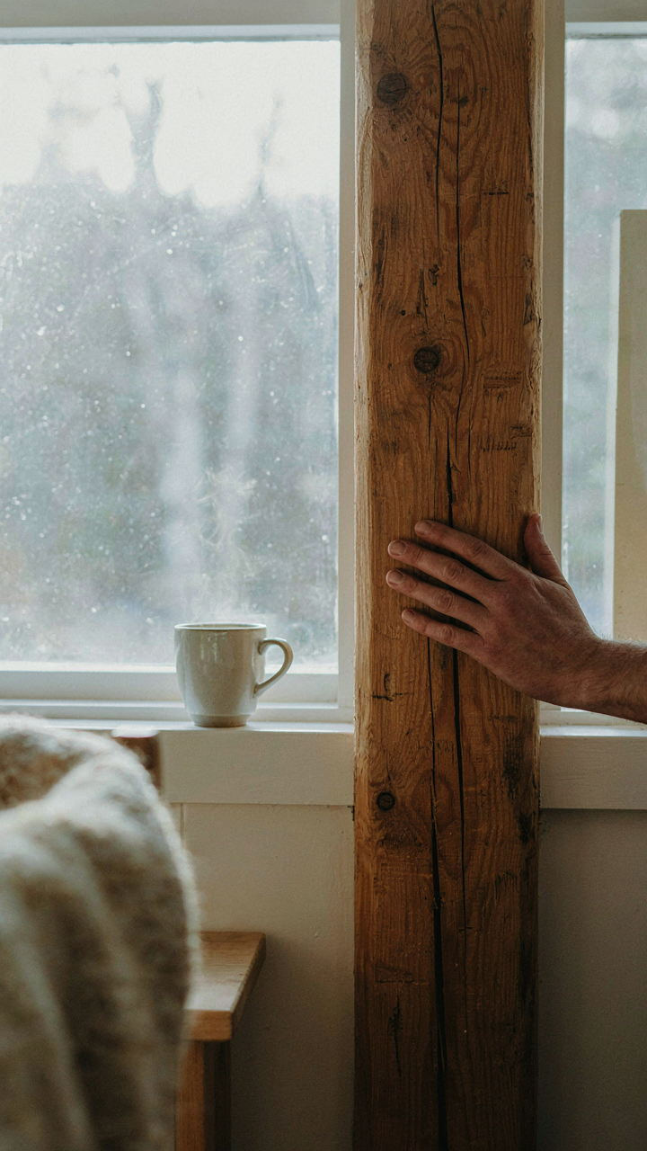 A hand touches a rough, untreated pine beam inside a scandinavian lake house.