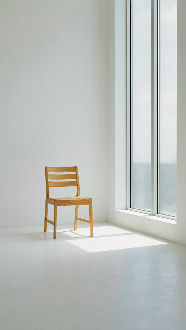 A single pale oak chair in a bright, empty minimalist room.