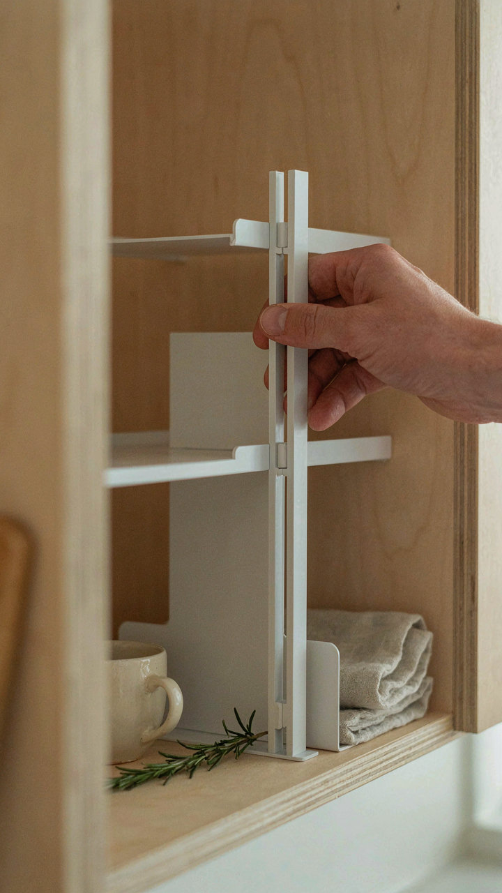 A hand adjusts a modular shelf divider in a kitchen cabinet.