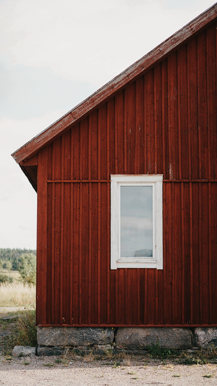 A scandinavian bungalow with weathered red board-and-batten siding and a granite foundation.