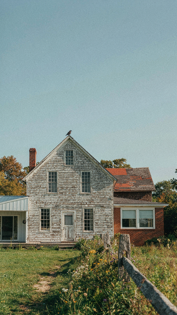 An old new england farmhouse shows multiple additions and varied window sizes over time.