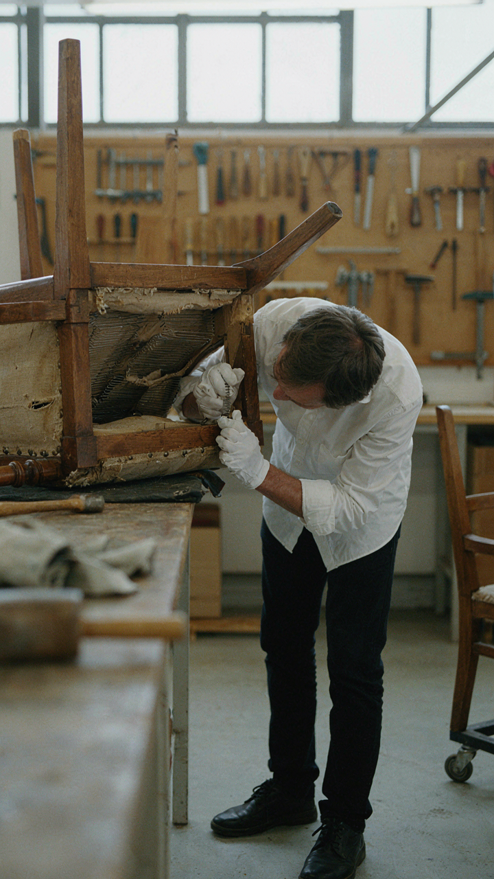 A conservator examines hand-tied springs under an antique chair.