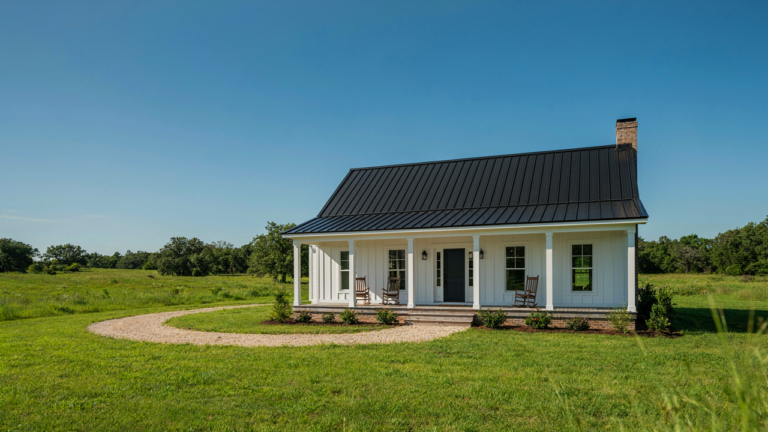 A beautiful new one story farmhouse stands in a field with a wide porch.