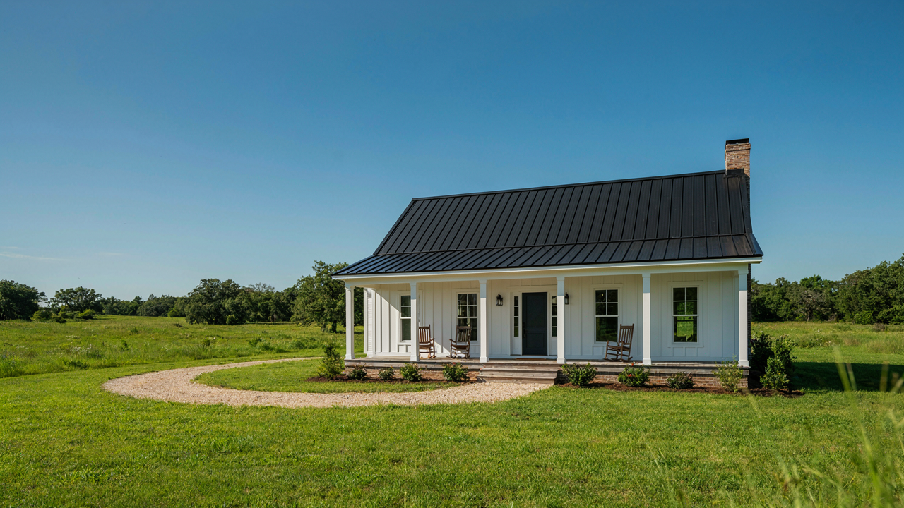 A beautiful new one story farmhouse stands in a field with a wide porch.