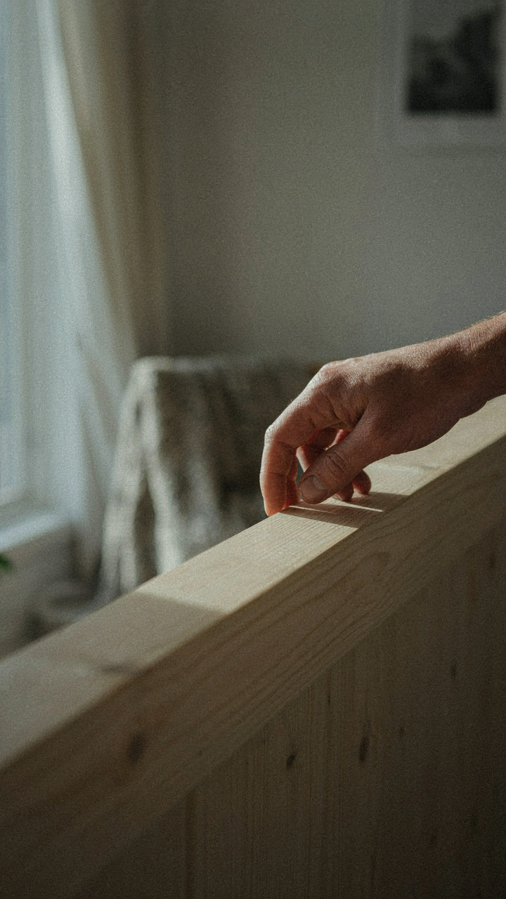 A hand touches a pale wood railing inside a Scandinavian cabin.