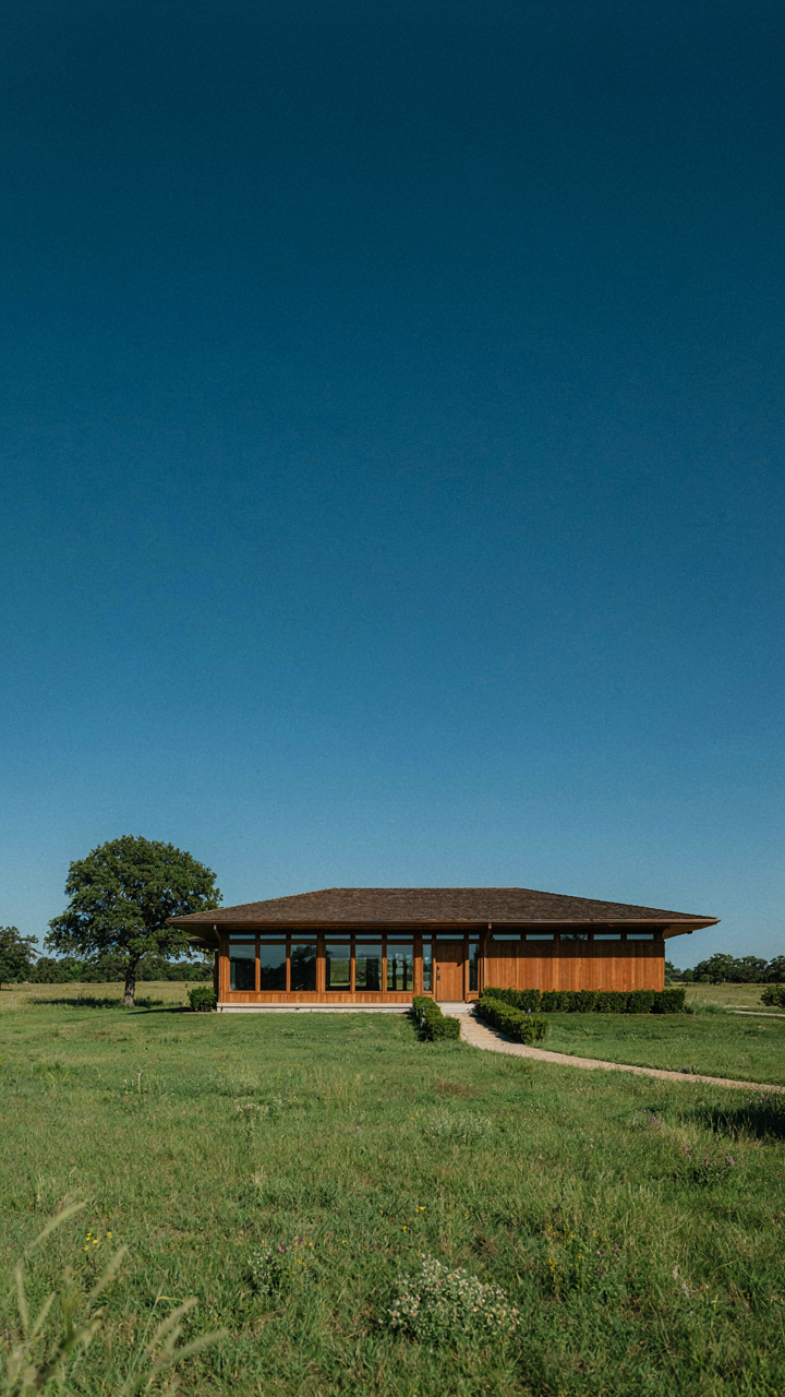A modern prairie style house with low sweeping rooflines, surrounded by green grass.