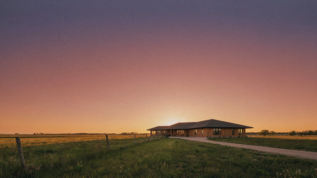 A wide prairie style house with a low sweeping roofline against a sunset over flat land.