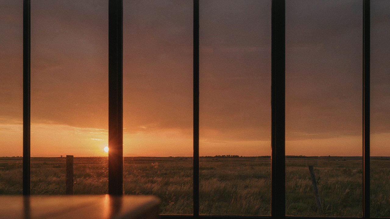 Wide prairie style windows framing a golden sunset over a vast landscape.