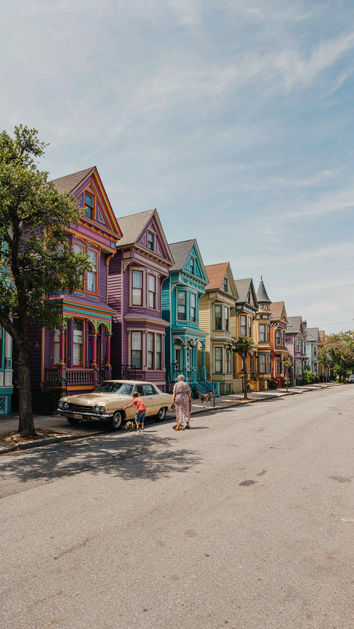 A purple Victorian house with rainbow trim on a street with other boldly colored homes.