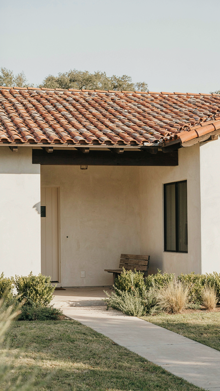 A ranch exterior with low shrubs, ground covers, and deep eaves casting shadows.