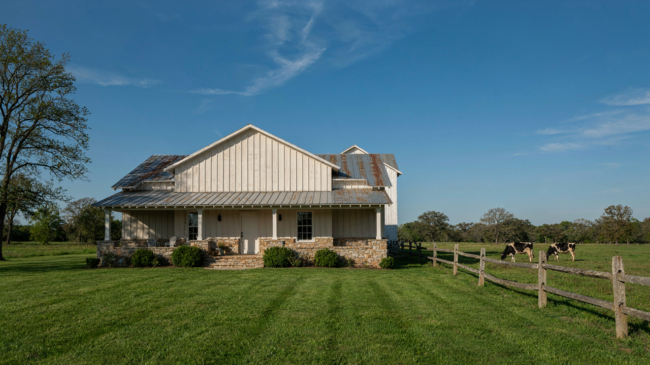 A modern ranch farmhouse with natural stone and wood siding, a low-slung roof, and deep eaves.