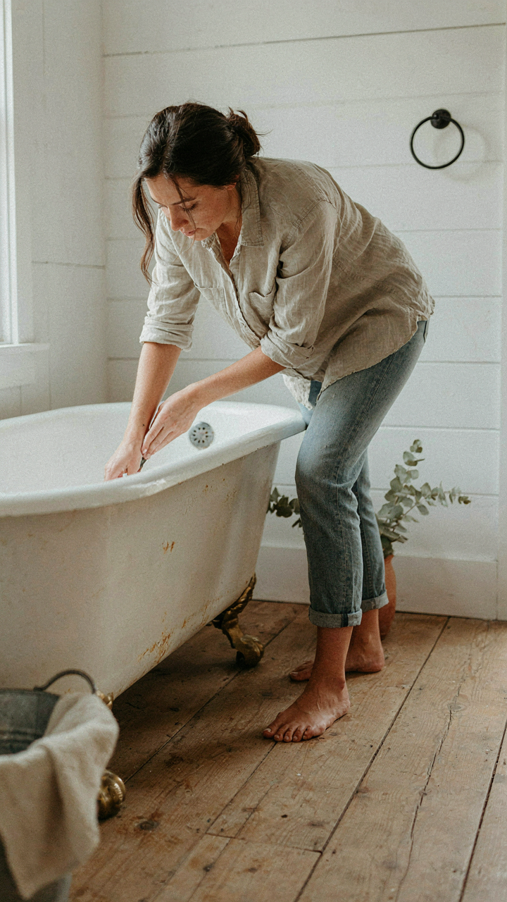 A person inspects a vintage cast iron tub for rust spots in a rustic bathroom.