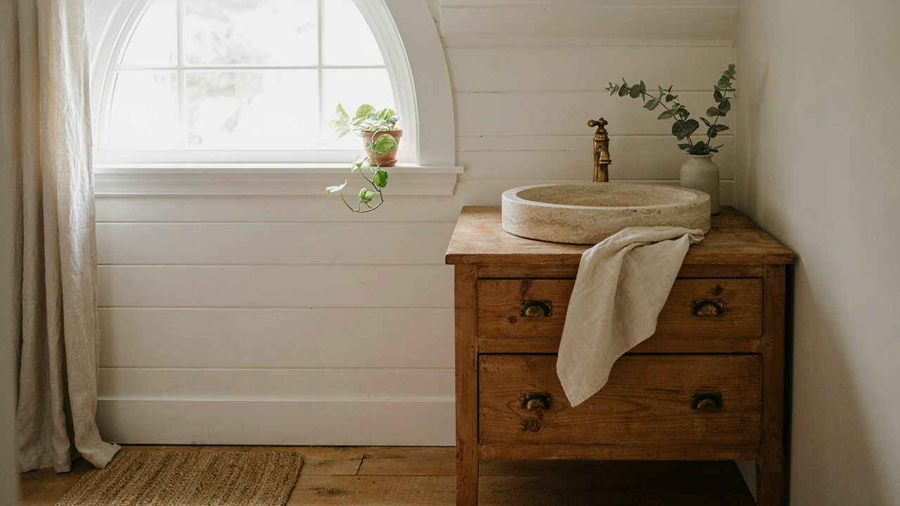 A charming rustic farmhouse bathroom featuring a worn wood vanity and stone basin.