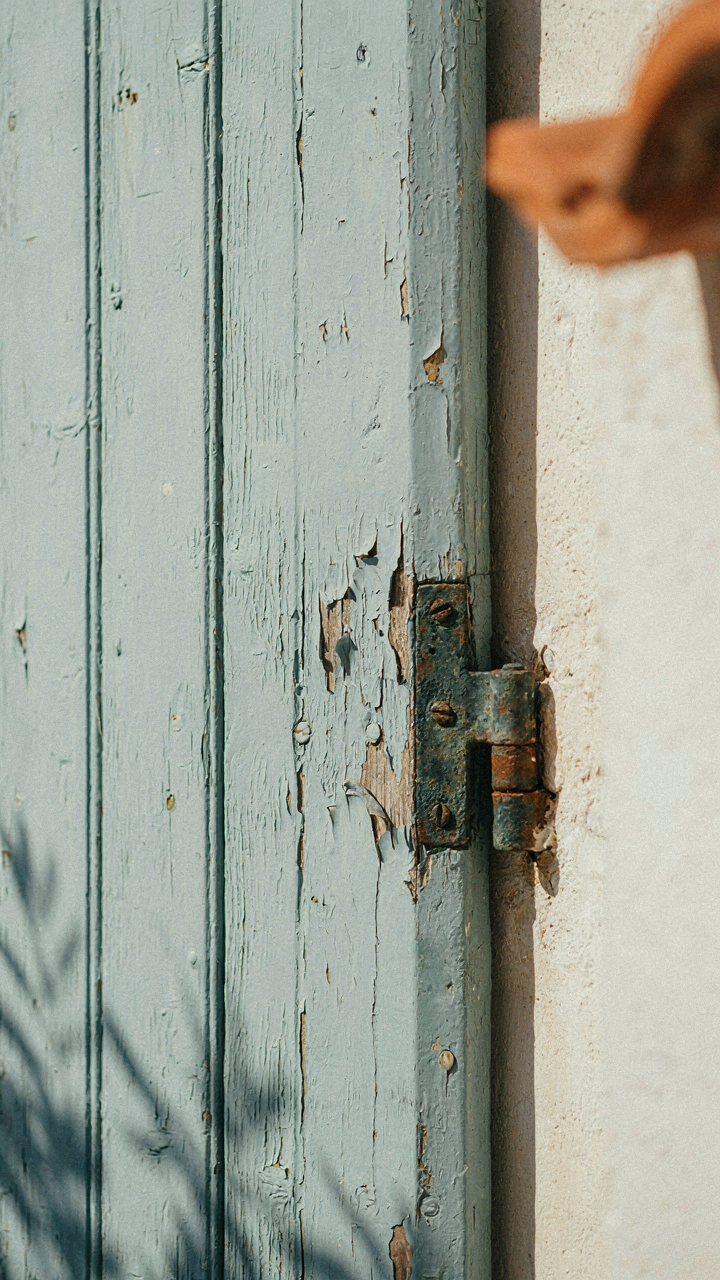 Old wooden shutter with peeling paint and patinated hinge.