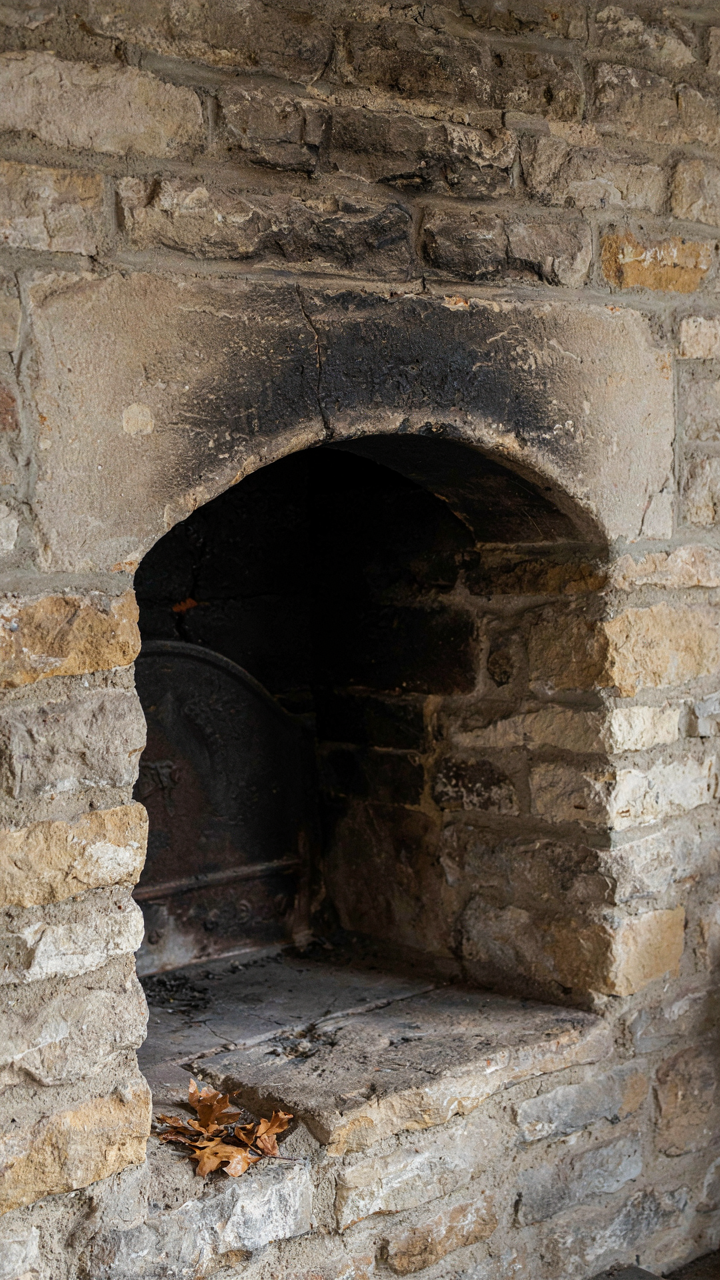 A close-up of an old, weathered stone fireplace with natural wear and soot.