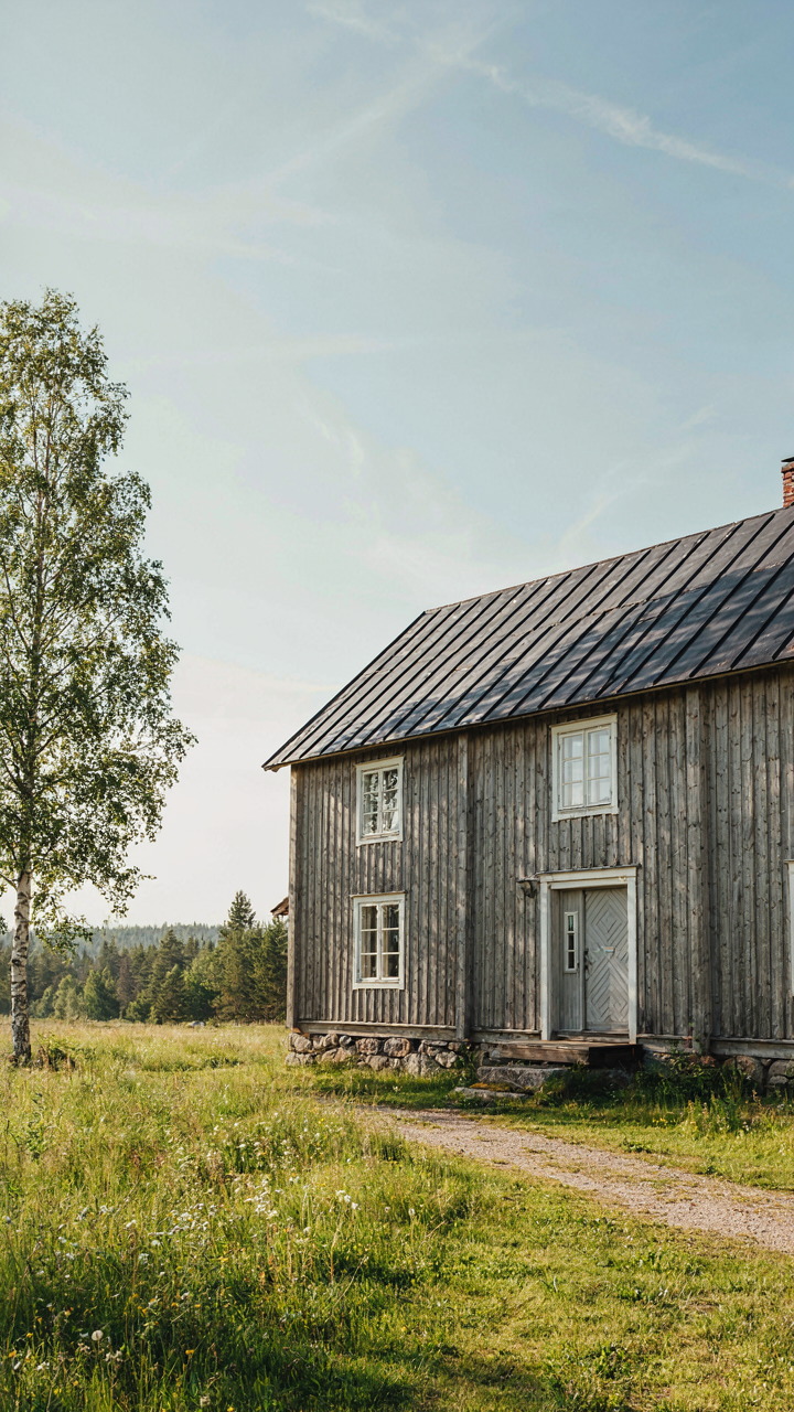 Exterior of a scandinavian farmhouse with weathered wooden siding and a stone foundation.