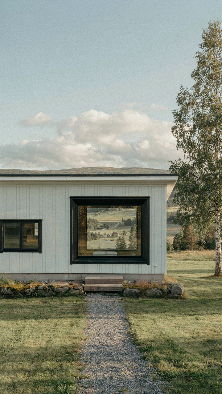 A small scandinavian bungalow frames a wide landscape view with a window.