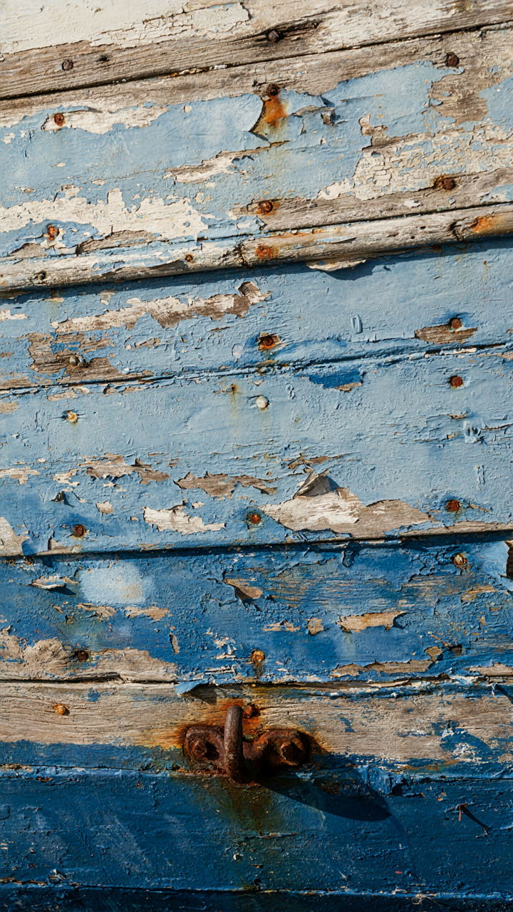 Overlapping layers of faded blue paint on an old boat hull.