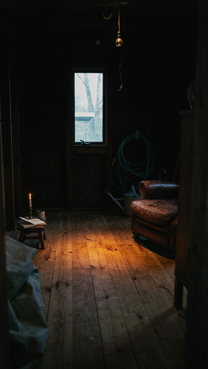 A cozy, circular pool of warm light on a wooden floor in a dimly lit she shed.