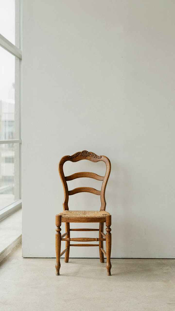 A single, beautifully carved wooden chair against a plain white wall.