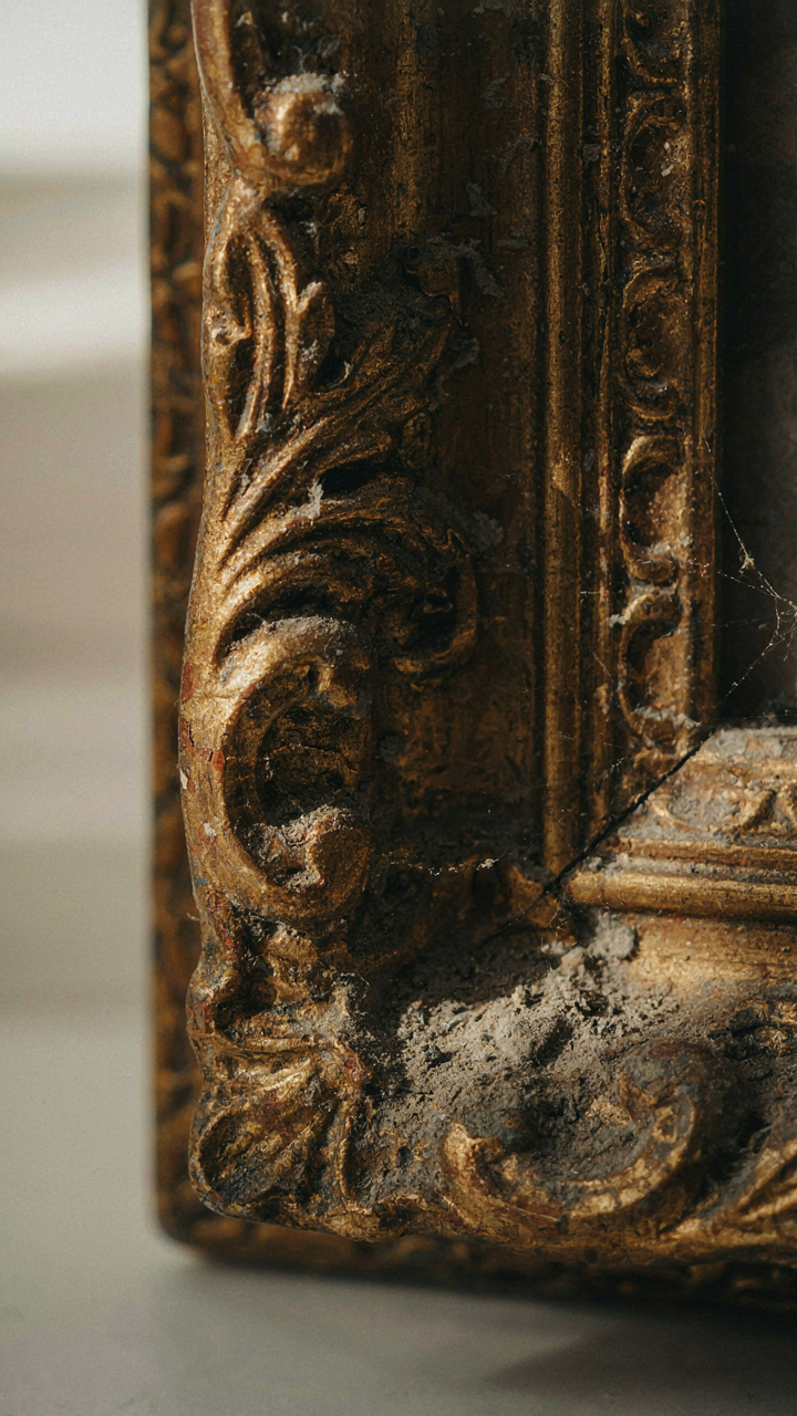 Dust collects in the intricate carvings of an ornate wooden frame.