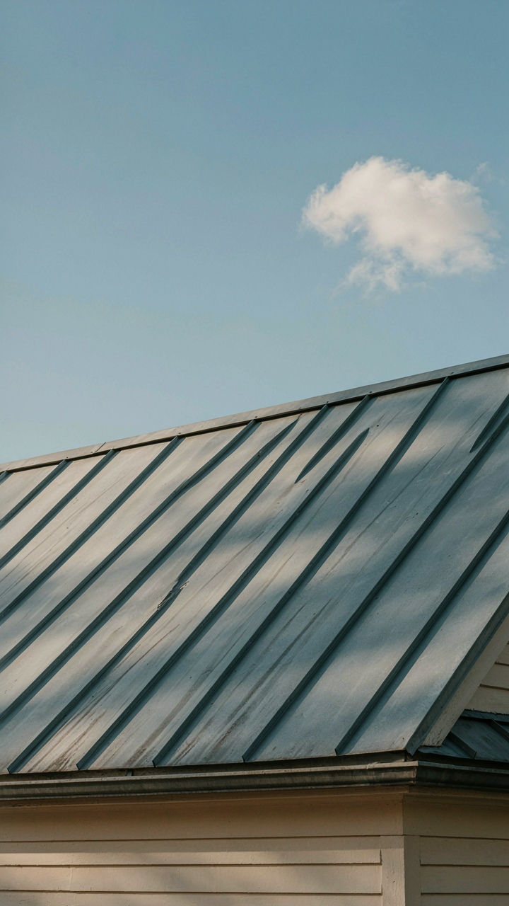 Well-maintained metal roof on a classic cottage bungalow under a blue sky.