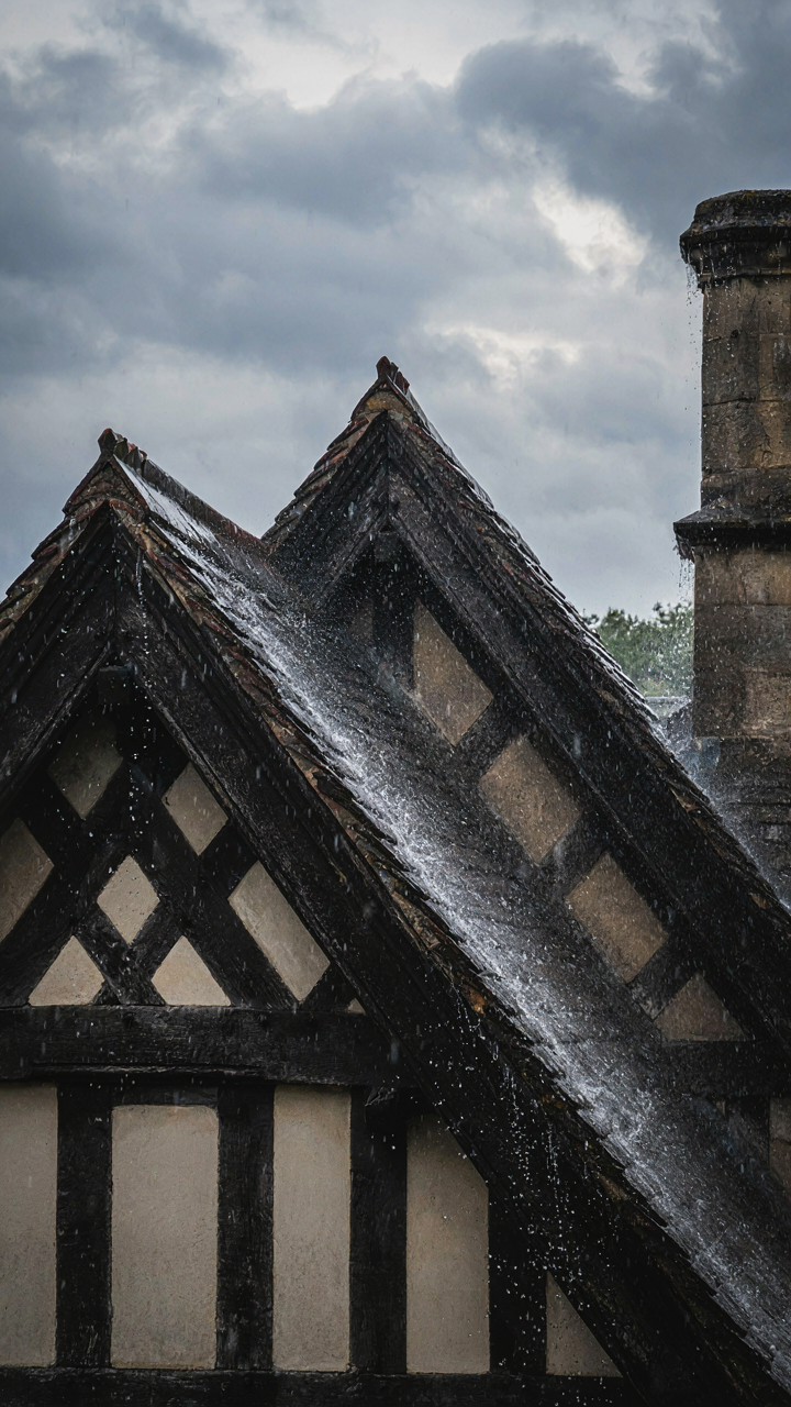 Rain runs fast off a steep roof of a tudor style house.
