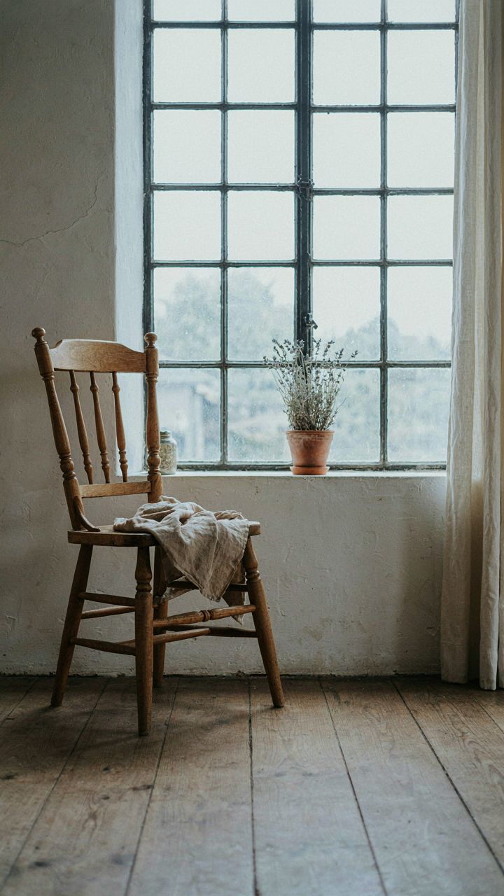 A single aged wooden chair by a window in an uncluttered French cottage room.