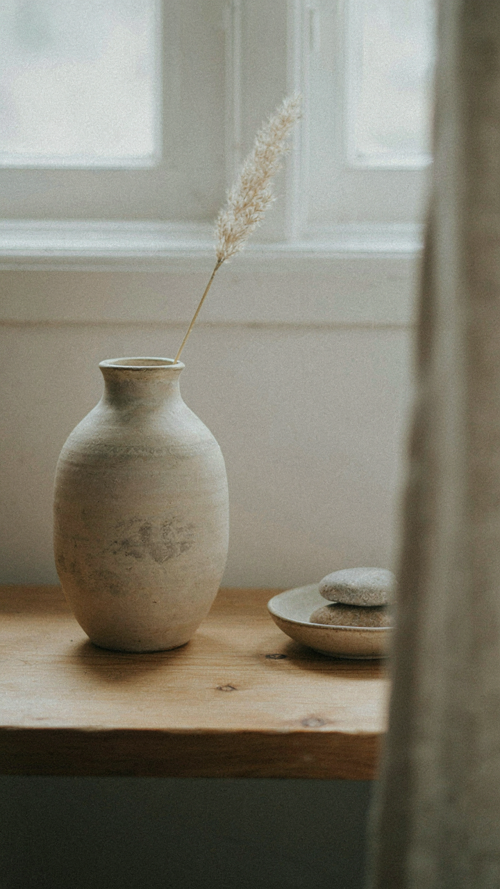 A single handcrafted ceramic vase on a bare pine shelf in a cottage interior.