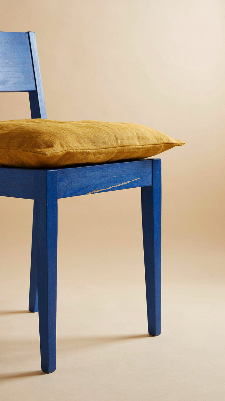 A painted wooden chair with a visible scratch and wrinkled linen cushion.