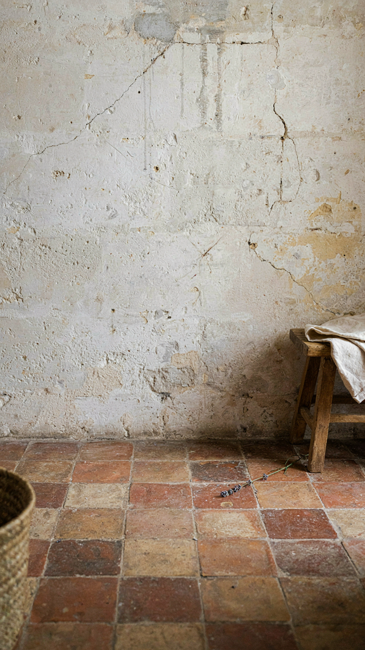A whitewashed stone wall and terra-cotta tile floor inside a French country interior.
