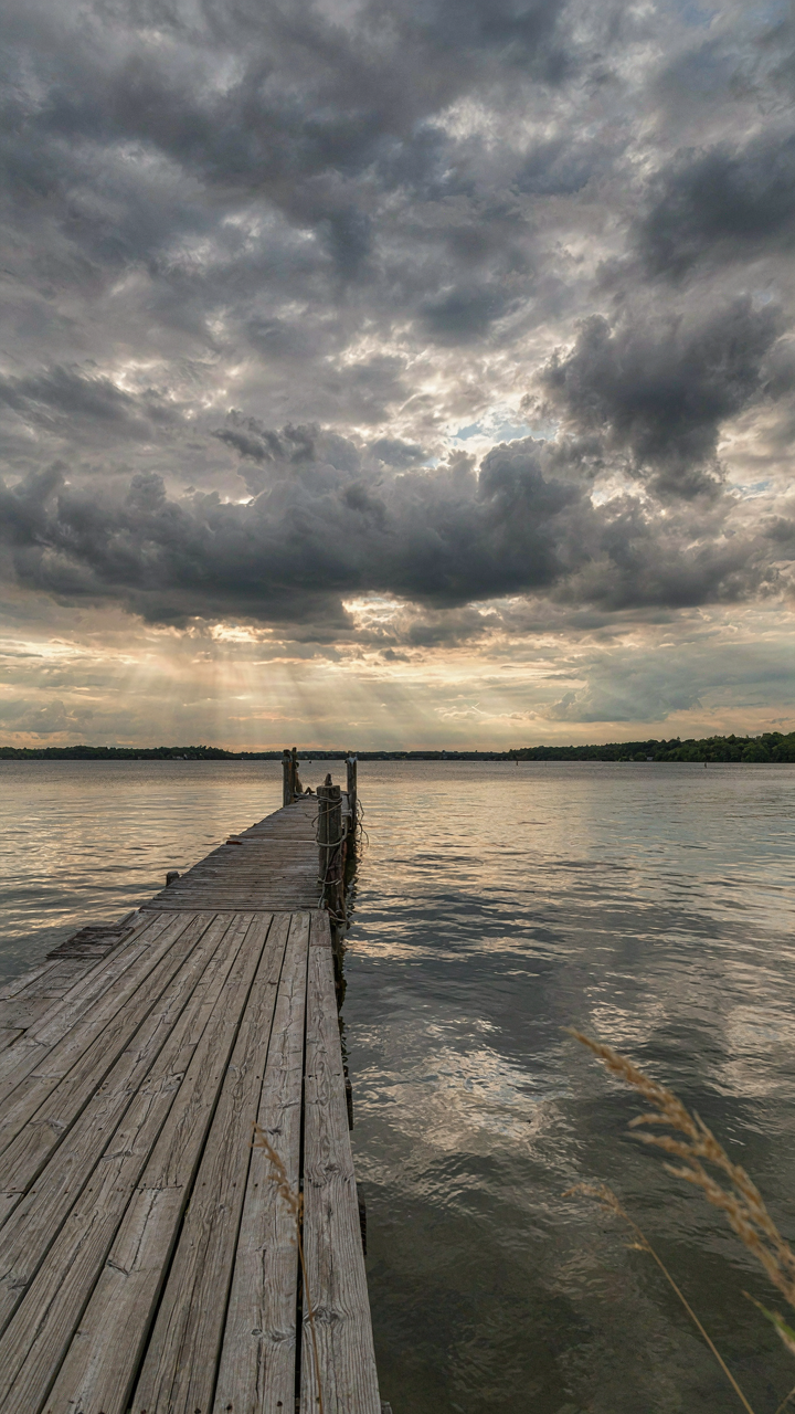 A weathered wooden dock under gray storm clouds at golden hour.