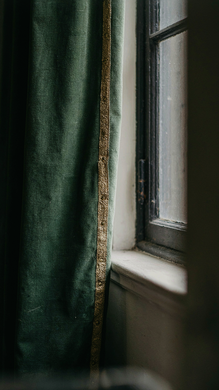 A close-up of a heavy, dark velvet curtain with ornate gold trim.