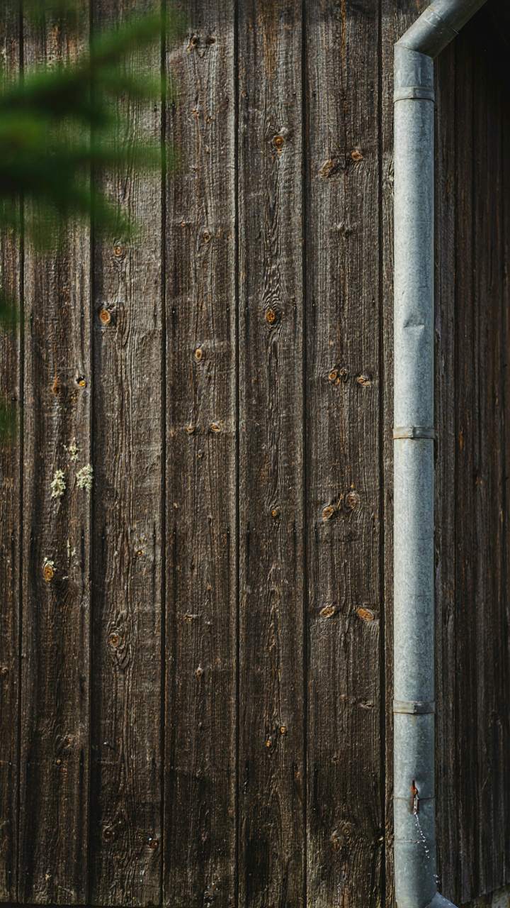 A weathered, dark cedar wall with a galvanized steel downspout on a cabin.