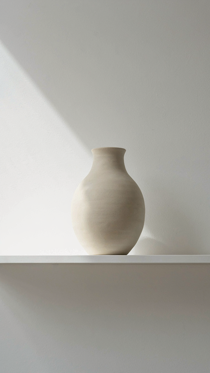 A single vase sits on a white shelf, with ample empty space around it.
